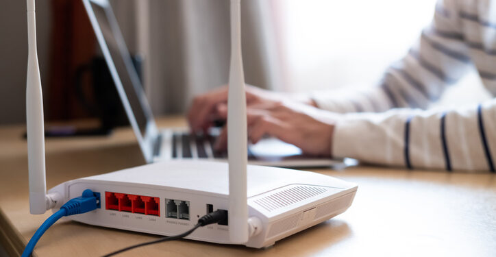Selective focus at router. Internet router on working table with blurred man connect the cable at the background. Fast and high speed internet connection from fiber line with LAN cable connection.