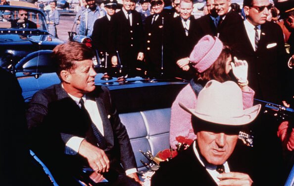 (Original Caption) Texas Governor John Connally adjusts his tie (foreground) as President and Mrs. Kennedy, in a pink outfit, settled in rear seats, prepared for motorcade into city from airport, Nov. 22. After a few speaking stops, the President was assassinated in the same car.