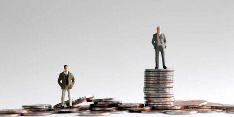 Miniature people standing on a pile of coins.